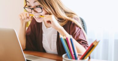 woman biting pencil while sitting on chair in front of computer during daytime